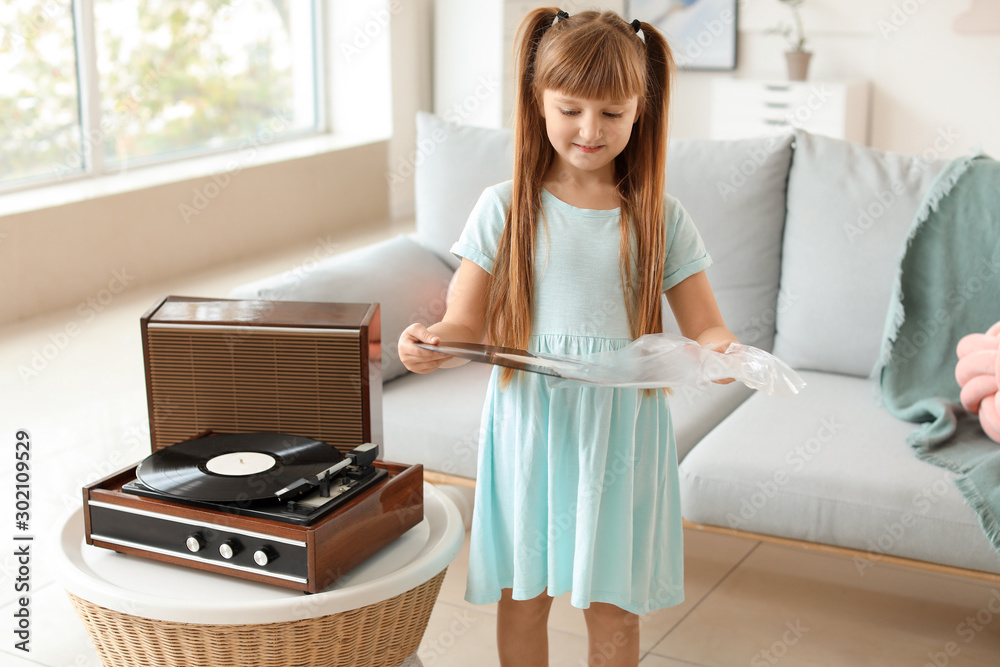 Cute little girl listening to music through record player at home