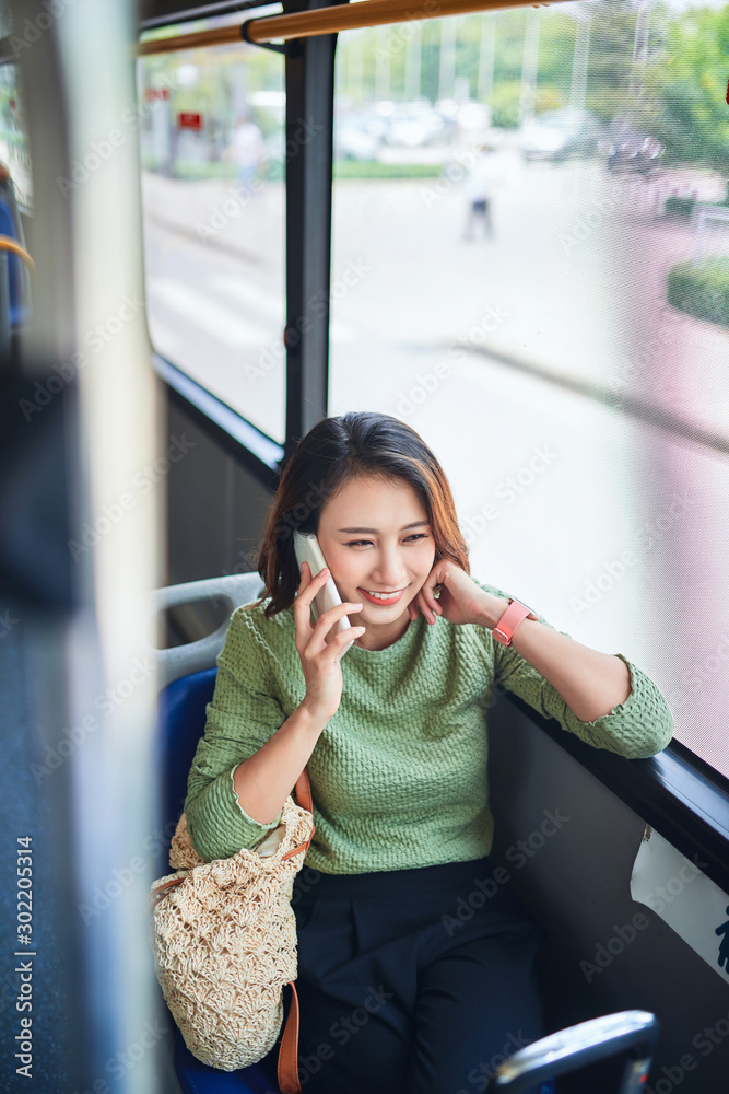 Asian woman sitting in city bus and talking on mobile phone.