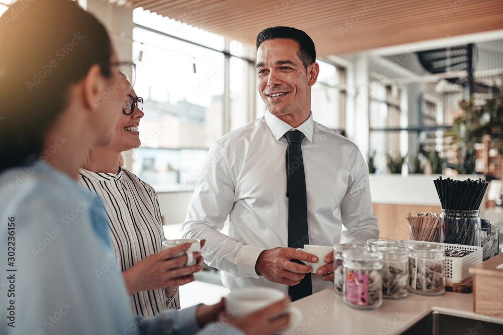 Laughing young businesspeople chatting together over coffee in a