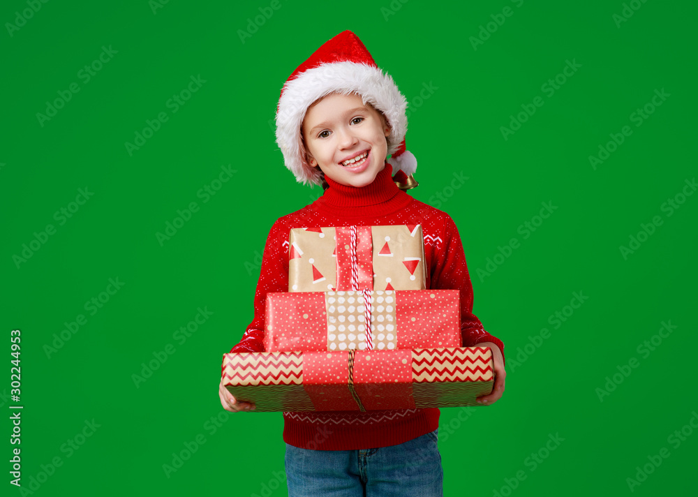 happy funny child girl in red Christmas hat   with gift on green   background.