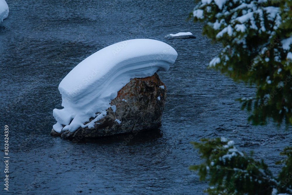 特写深蓝色溪流中央的大岩石被新鲜的雪覆盖