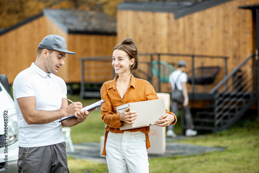 Couriers delivering goods to a young woman home by cargo van vehicle, workman moving cardboard parce