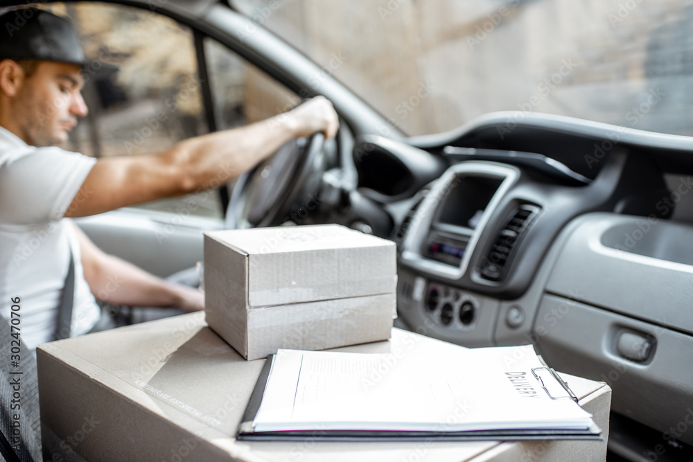 Delivery man driving cargo vehicle with parcels on the passenger seat, image focused on the cardboar