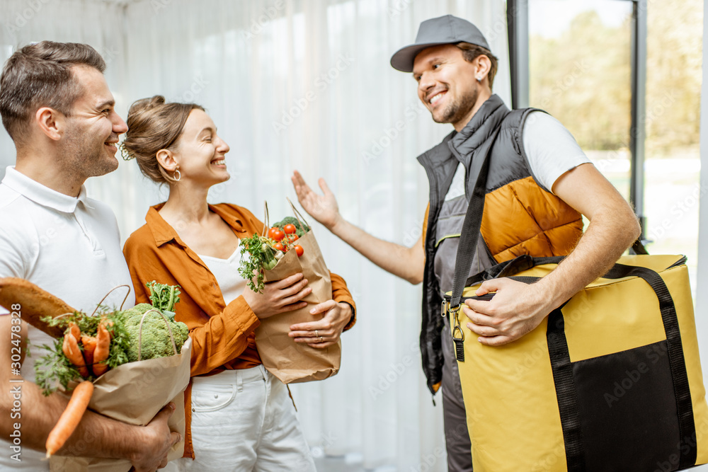 Cheerful courier in uniform delivering fresh groceries to a young family home. Online shopping and h