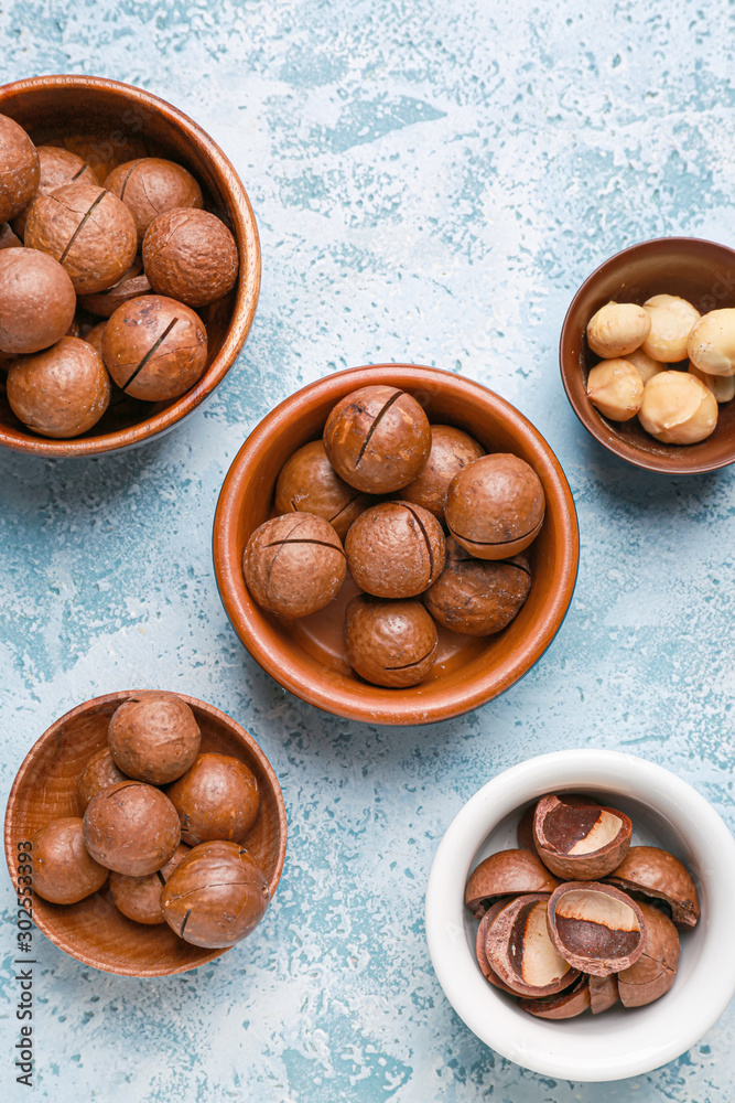 Bowls with macadamia nuts on color background