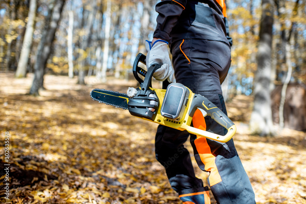 Professional lumberjack in protective workwear walking with a chainsaw in the forest, close-up on a 