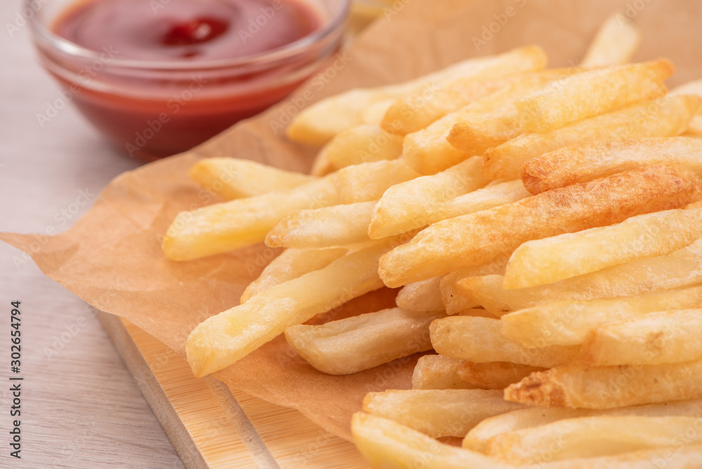 Golden yummy deep French fries on kraft baking sheet paper and serving tray to eat with ketchup and 