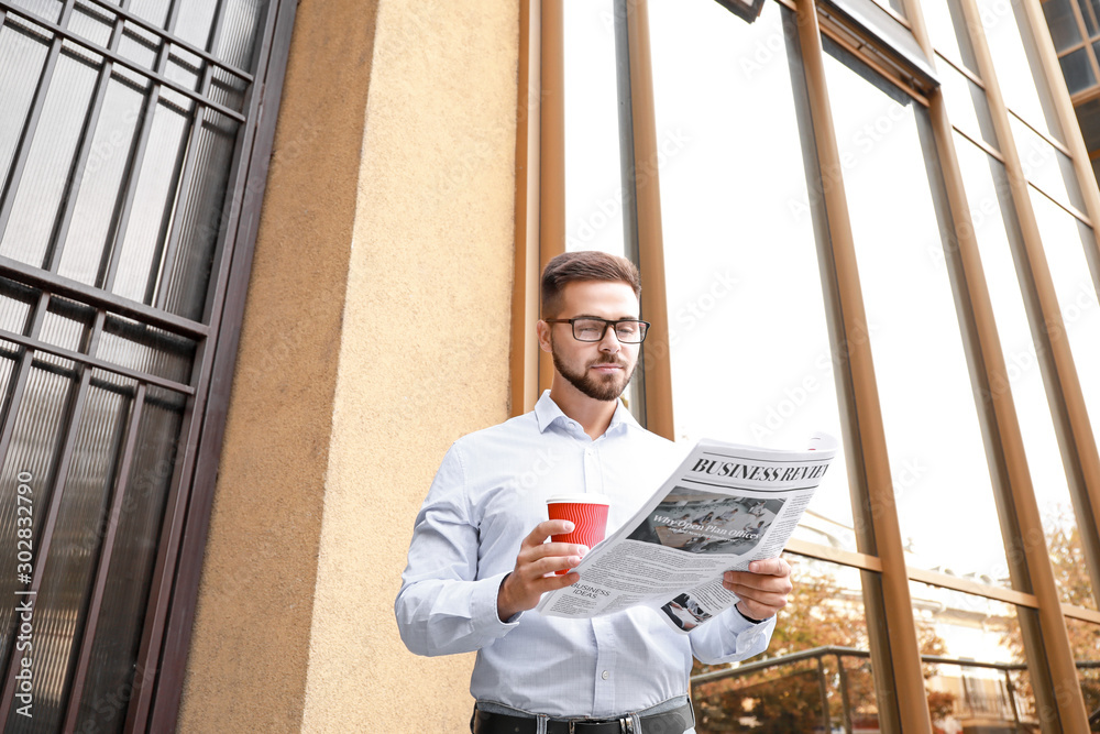 Handsome man with newspaper and cup of coffee outdoors