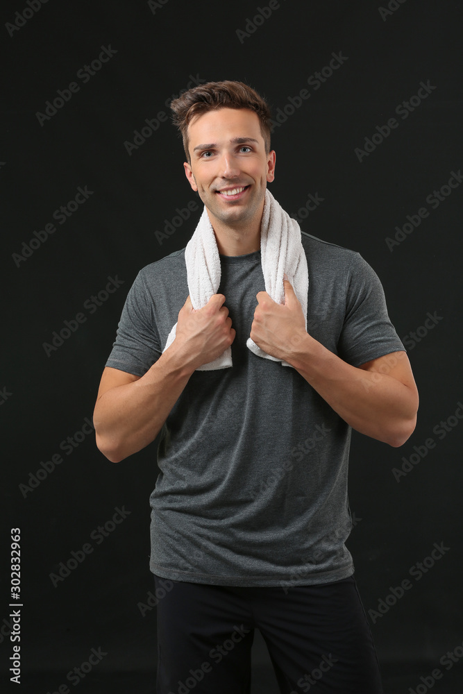 Sporty young man with towel on dark background