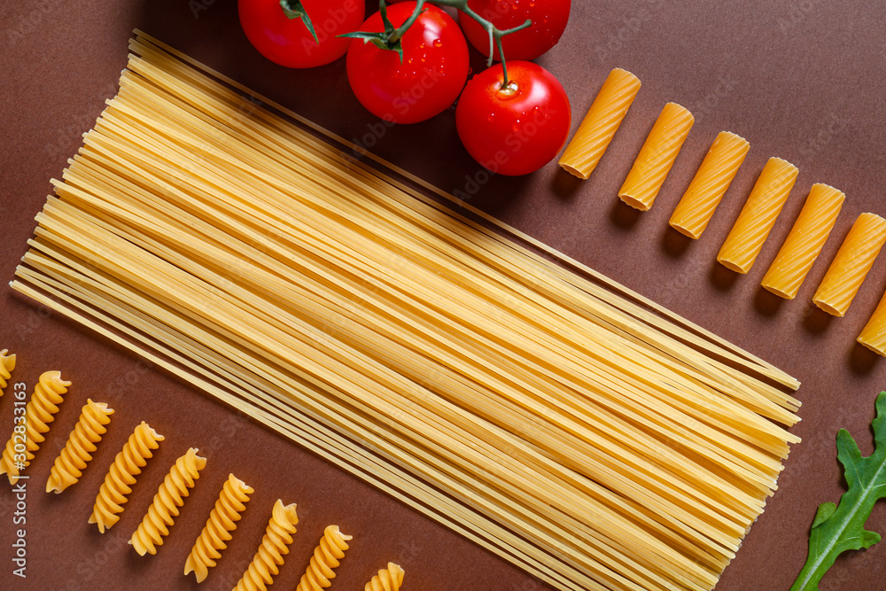 Different dry pasta with fresh tomatoes on color background