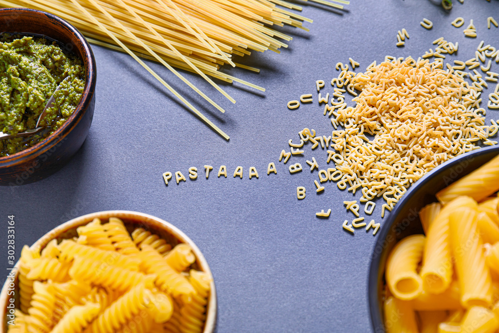 Different dry pasta with pesto sauce on color background