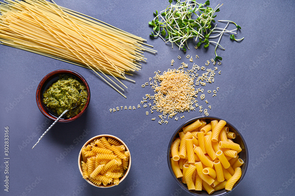 Different dry pasta with pesto sauce and sprouts on color background