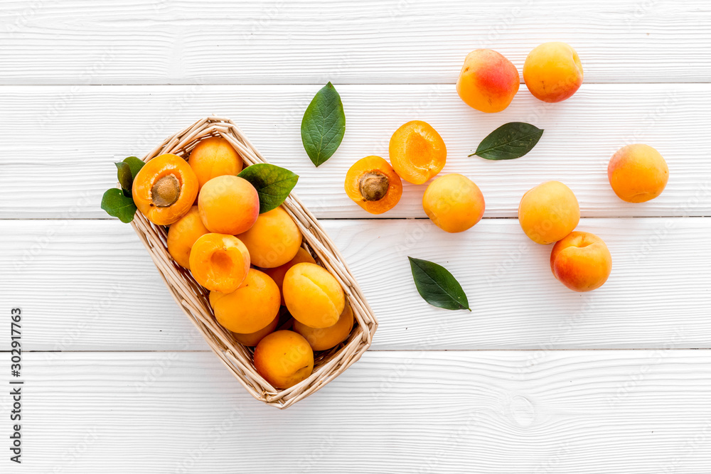 Fresh raw apricots in basket on white wooden background top view pattern with leaves