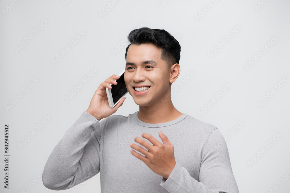 Thoughtful happy asian man smiling while talking on mobile phone isolated against white background`