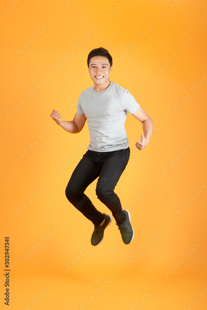 Energetic happy young Asian man in casual clothes jumping, studio shot isolated in orange background