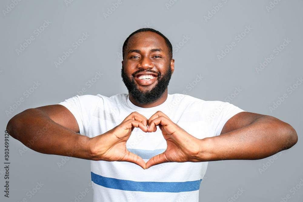 Happy African-American man showing heart shape with hands on grey background