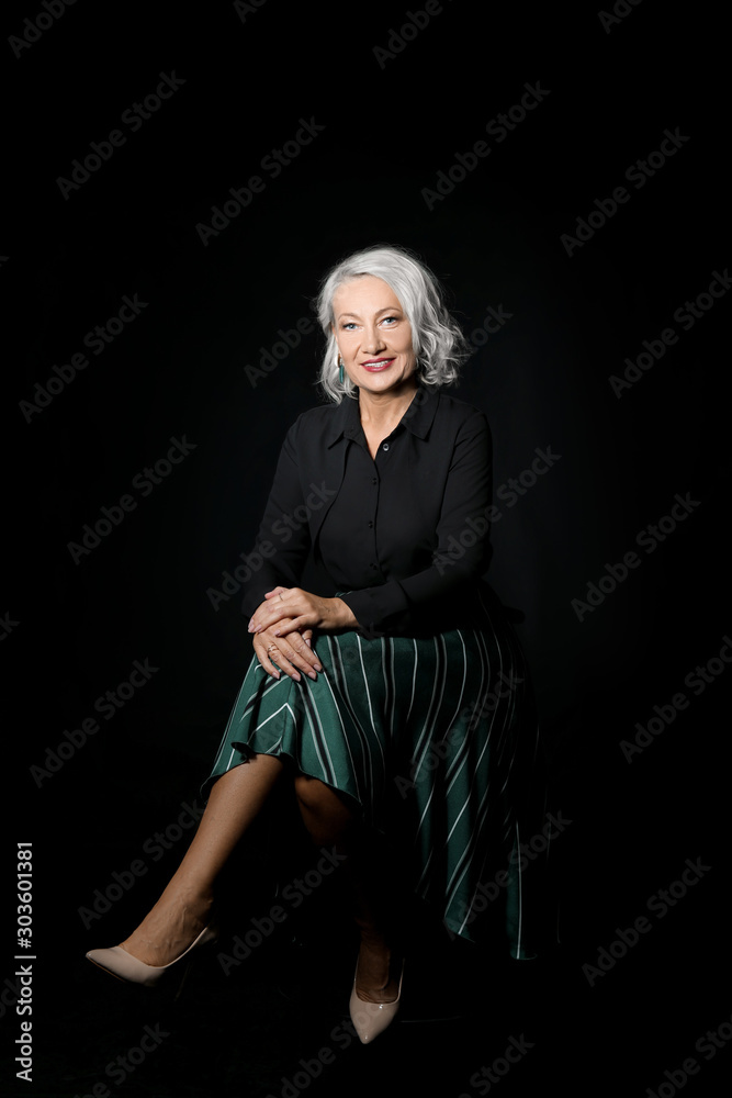 Portrait of stylish mature woman sitting on chair against dark background