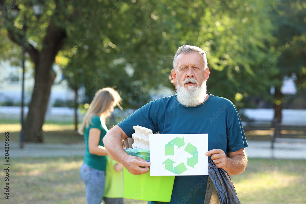 Man holding gathered garbage and paper sheet with symbol of recycling outdoors