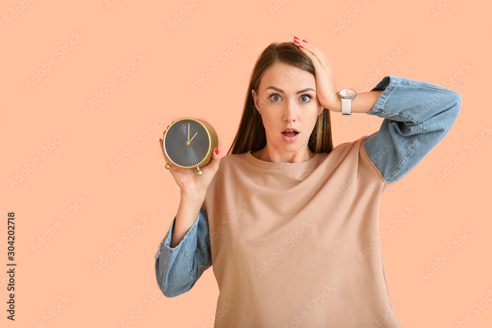 Stressed young woman with alarm clock on color background