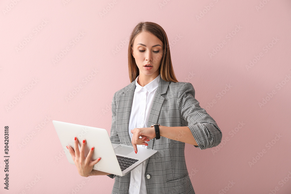 Businesswoman with laptop looking at watch on color background