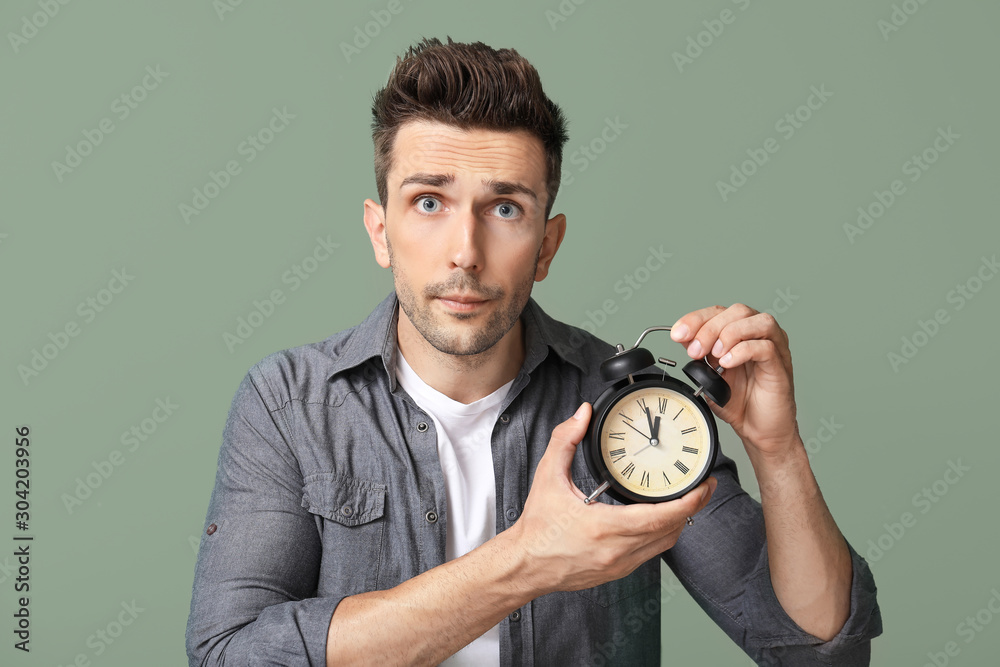 Handsome young man with alarm clock on color background