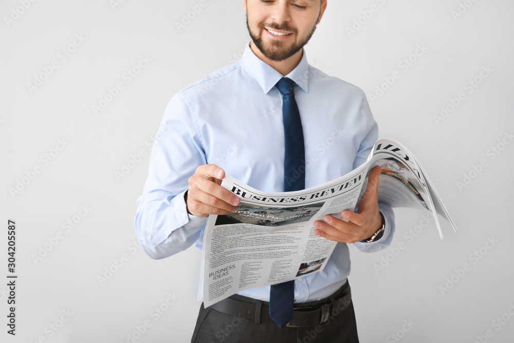 Handsome businessman with newspaper on light background