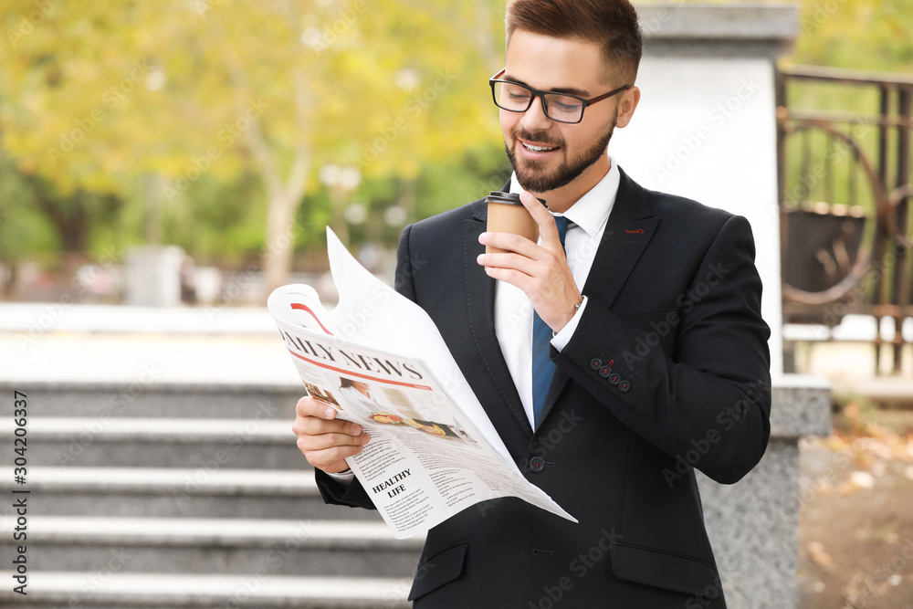 Handsome businessman with newspaper and coffee outdoors