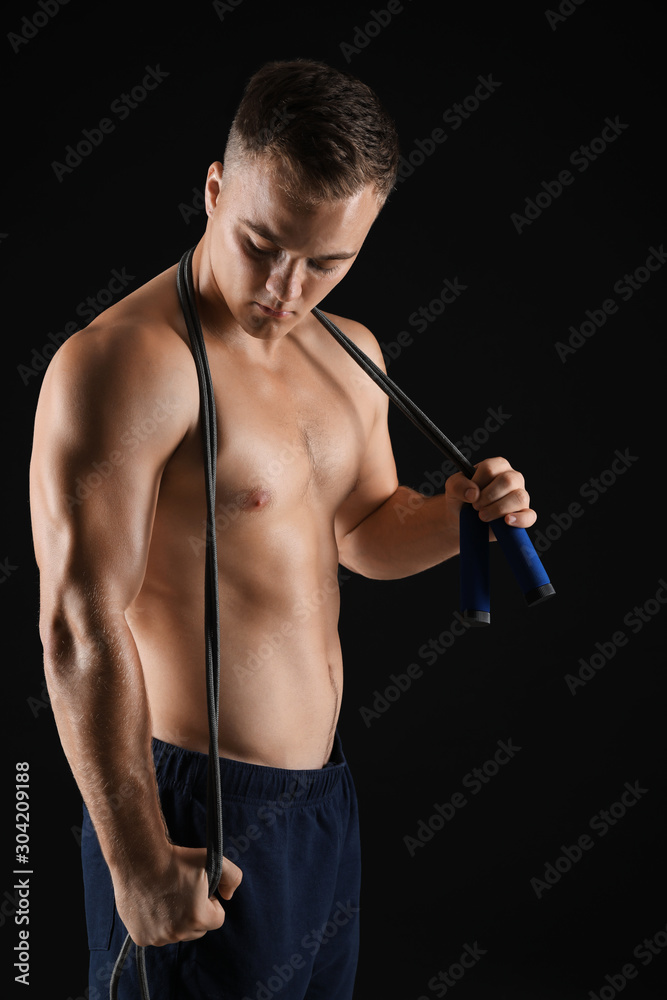 Handsome male bodybuilder with jumping rope on dark background