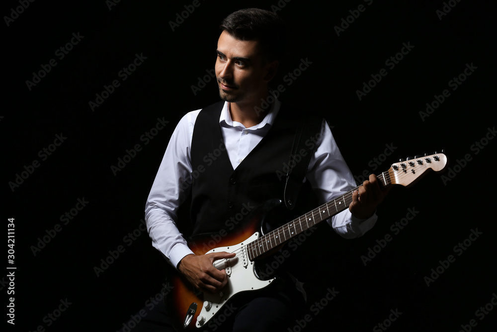 Handsome man playing guitar on dark background