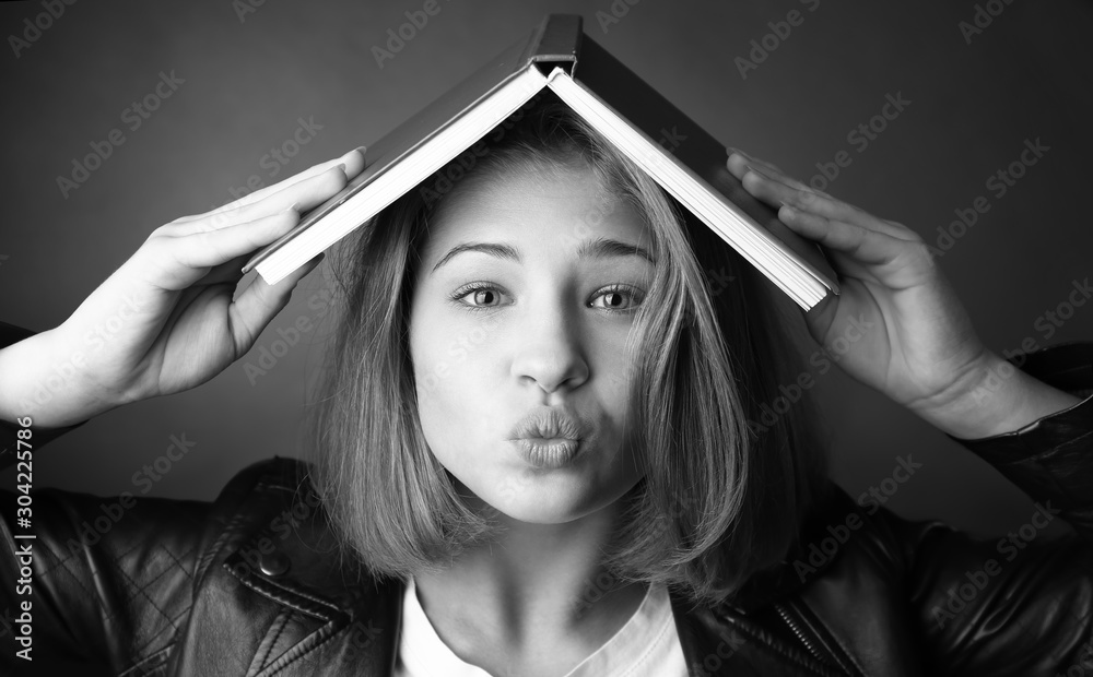 Black and white portrait of funny teenage girl with book on dark background