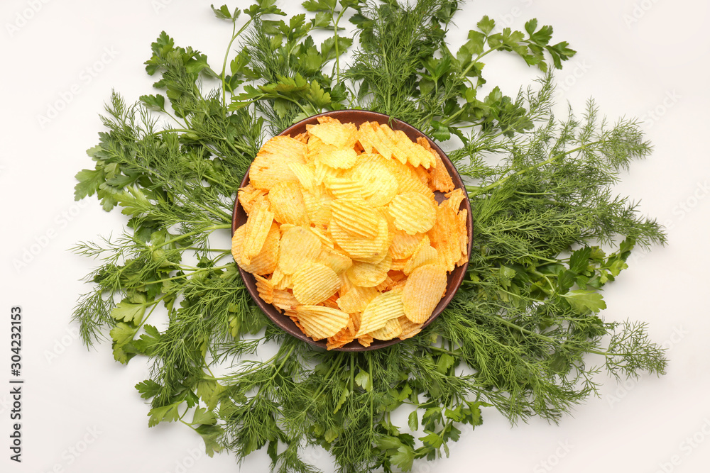 Bowl with tasty potato chips and herbs on table