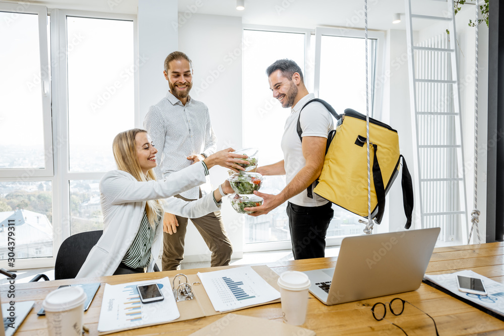 Courier delivering healthy business lunches with thermal bag for the office employees, giving them t