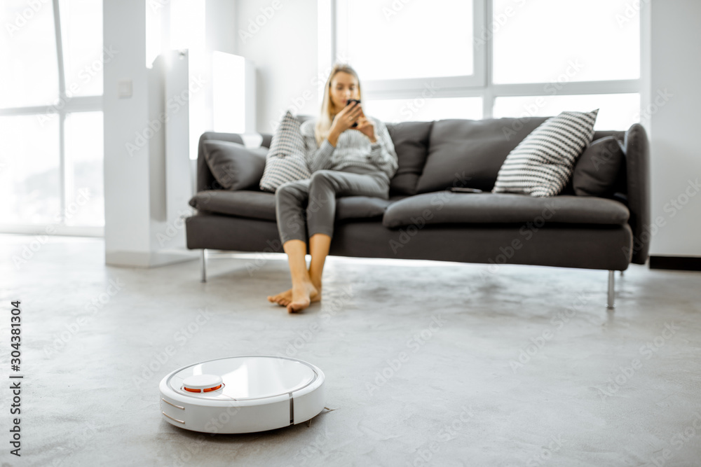 Woman relaxing on the couch while automatic vacuum cleaner doing the housework in the modern white l