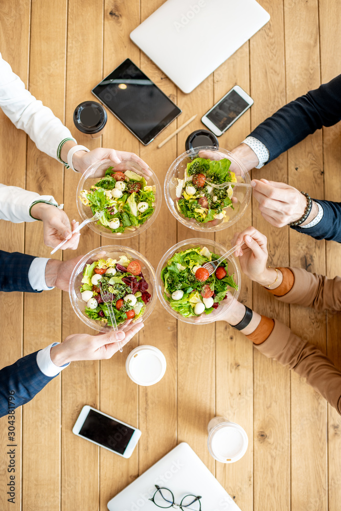 Office workers during a business lunch with healthy salads and coffee cups, view from above on the w