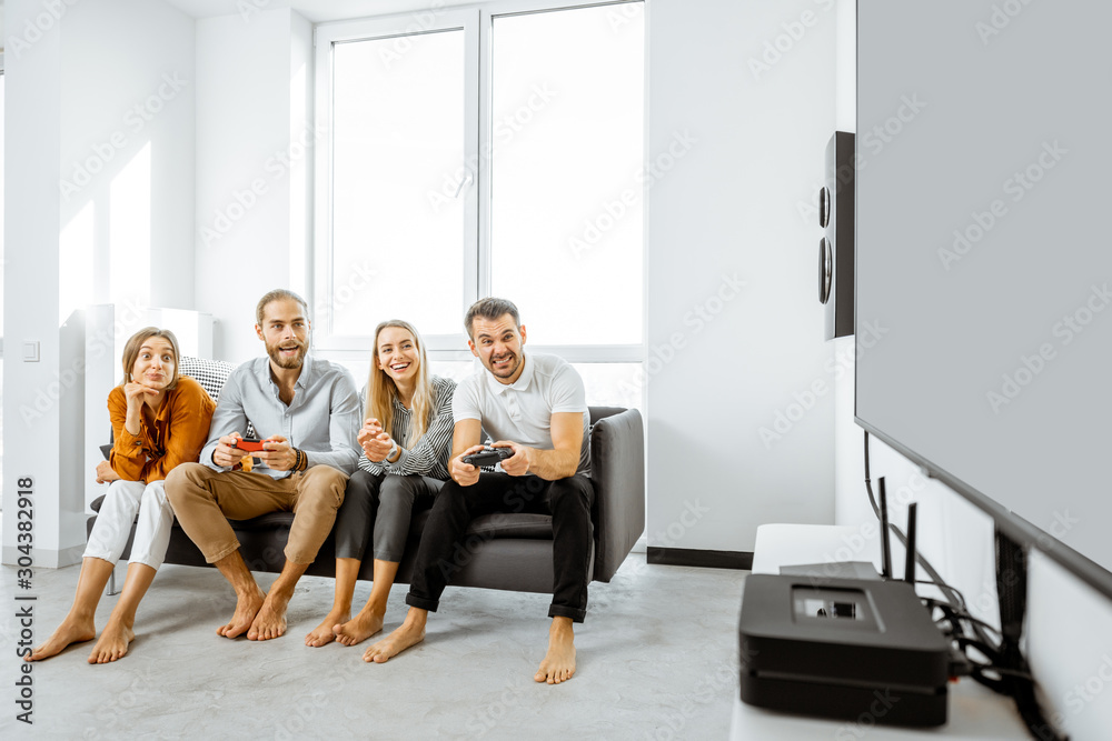 Group of a young friends having fun while playing video games on the couch at home. Wide view with l