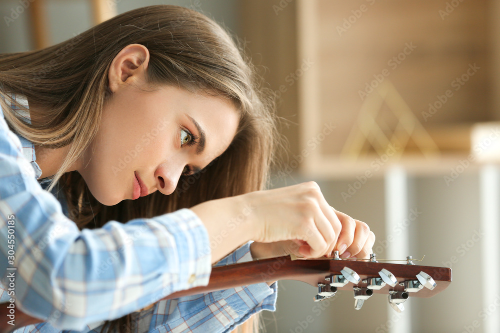 Young woman tightening strings of guitar at home