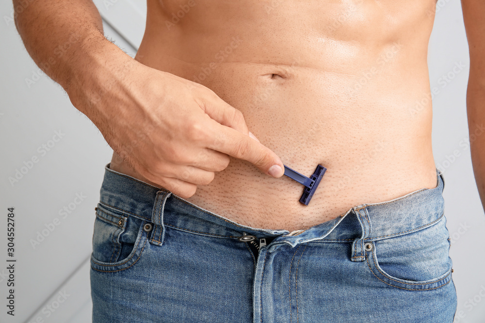 Handsome young man shaving his body on light background, closeup