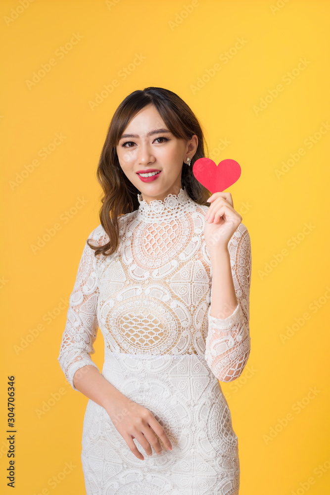 Portrait of young beautiful asian woman hands holding red heart shape isolated on yellow background.