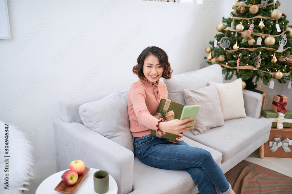 christmas concept - young woman taking selfie photo near decorated christmas tree