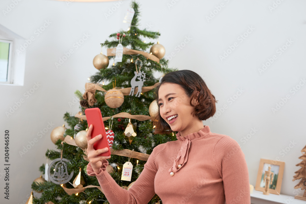 节日、冬天和人的概念——快乐的年轻女人在家里的圣诞树附近自拍