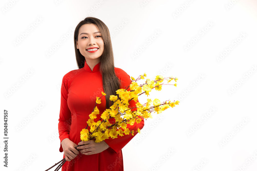 Asian young girl wearing traditional clothing (ao dai), holding a branch of yellow Apricot blossom.