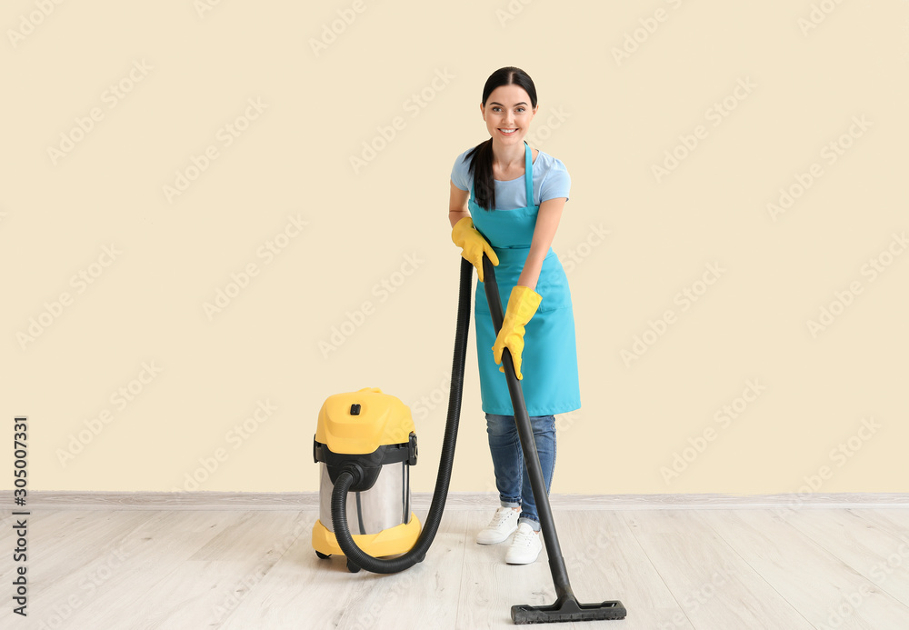 Female janitor with vacuum cleaner against light wall