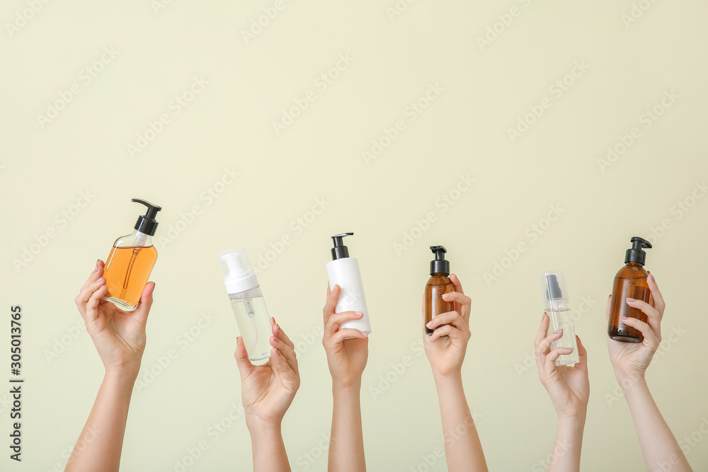 Female hands with different cosmetic products in bottles on color background