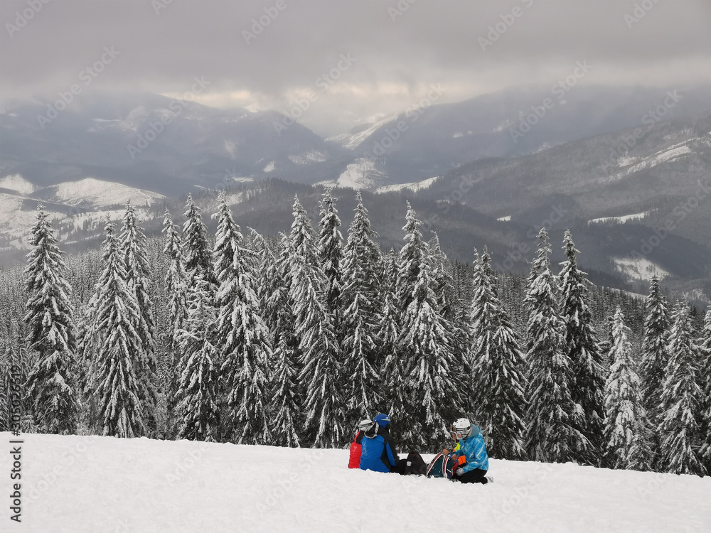 穿着滑雪服的滑雪者坐在雪地上。在山顶休息