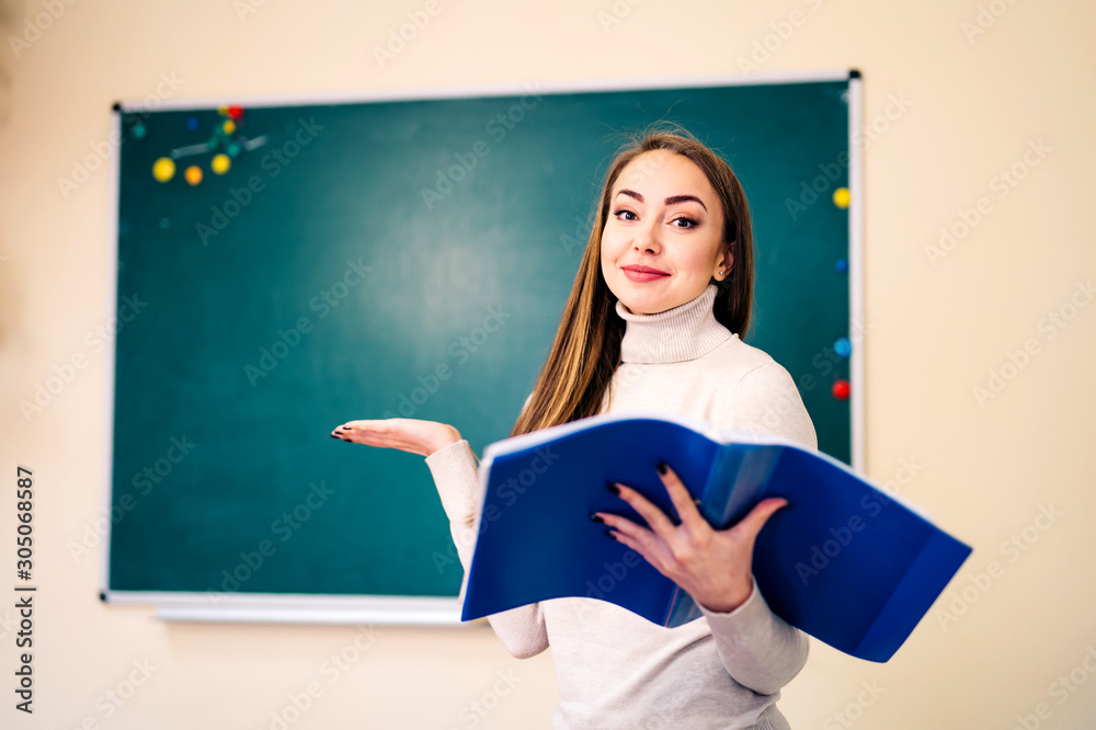 Student girl standing near clean blackboard in the classroom with open notes in hands. School and ed