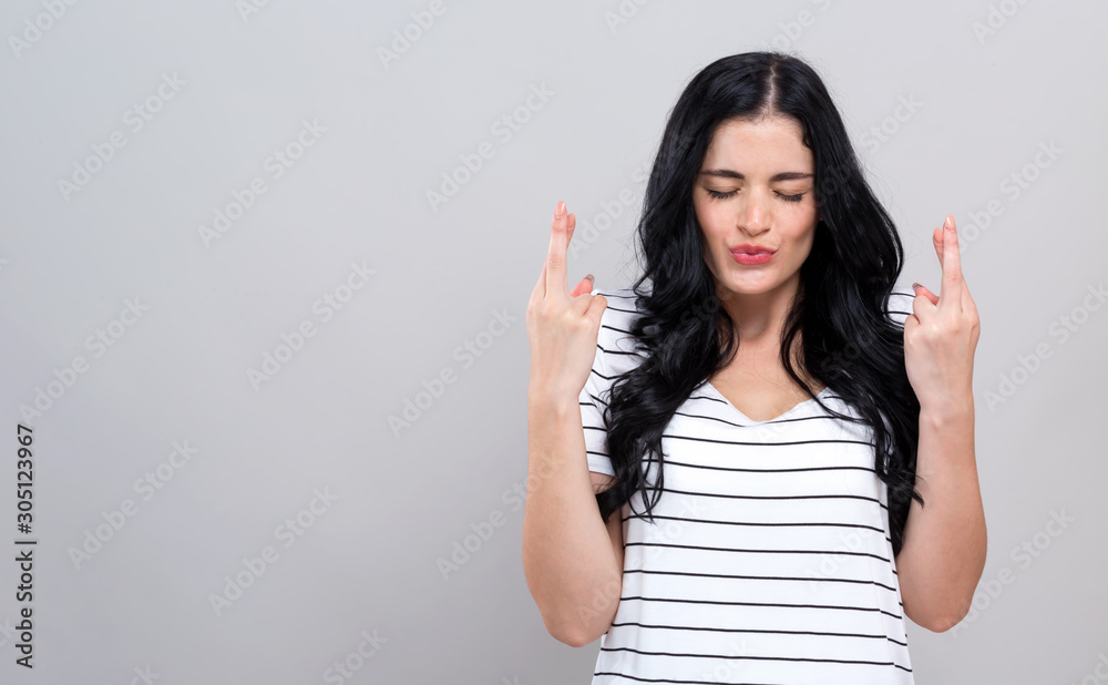 Young woman crossing her fingers and wishing for good luck on a gray background