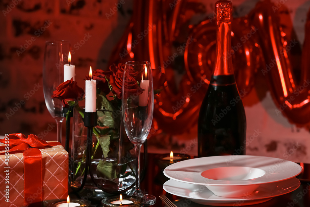 Champagne, flowers, gift and plates on table prepared for romantic dinner on Valentines Day