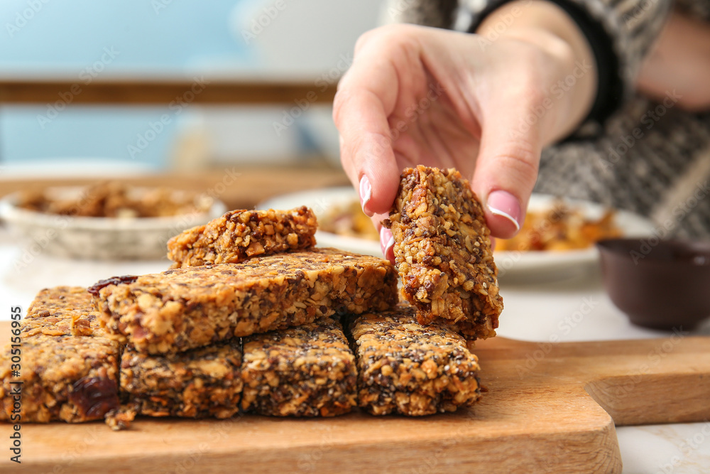 Woman taking tasty granola bar from table, closeup