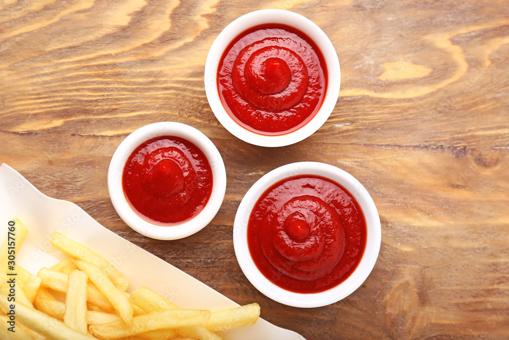 Tasty french fries and tomato sauce on wooden background