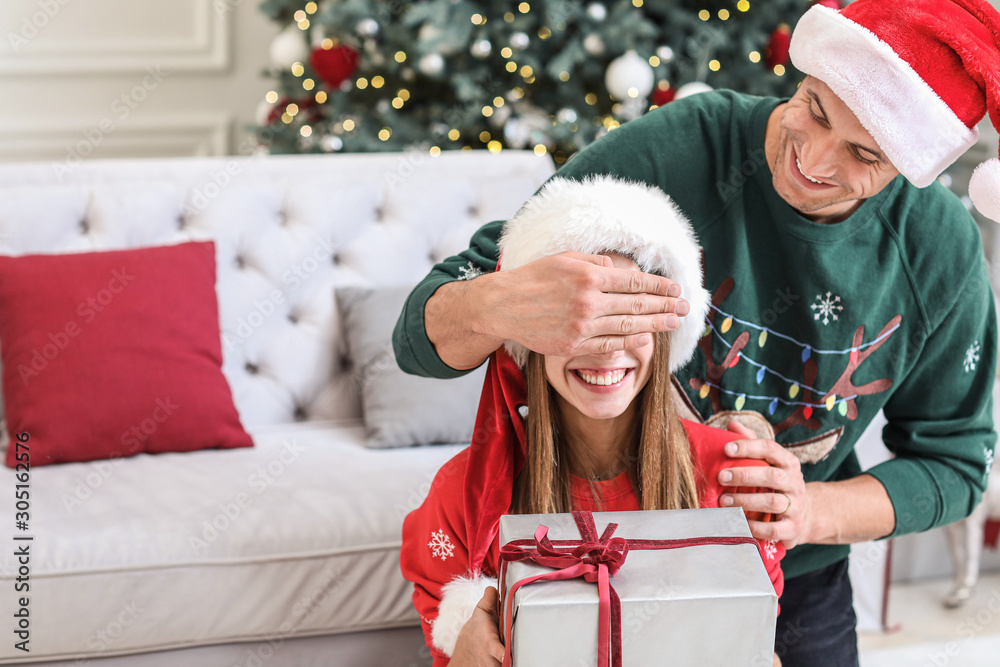 Happy young man giving Christmas present to his girlfriend at home